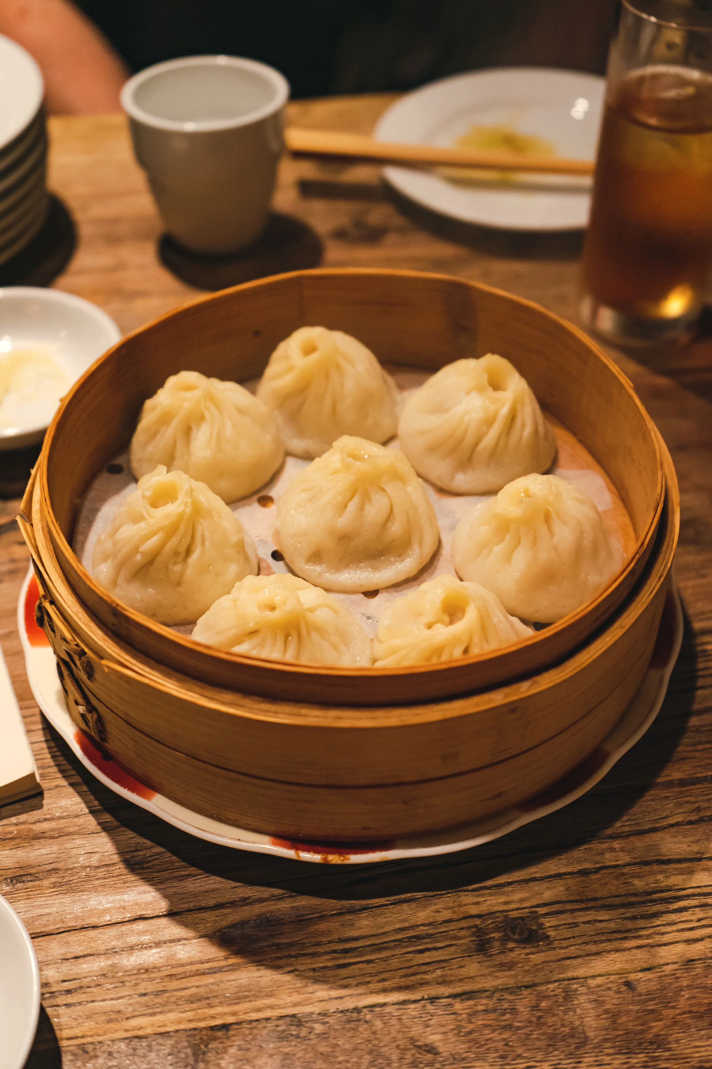 Soup dumplings in a bamboo steamer basket with dipping vinegar